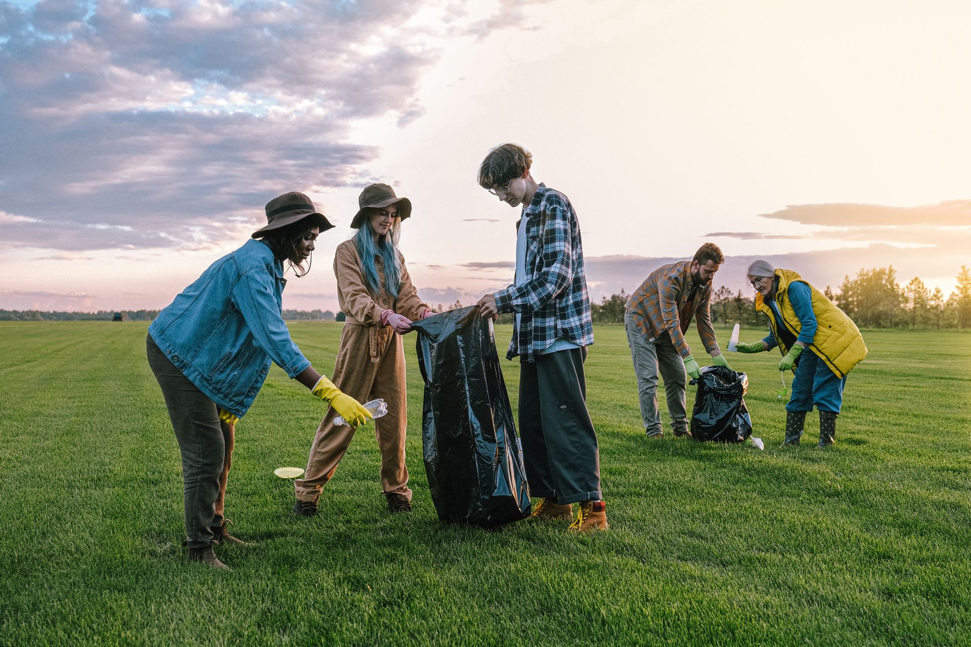 Volunteers collecting litter in a field at sunset